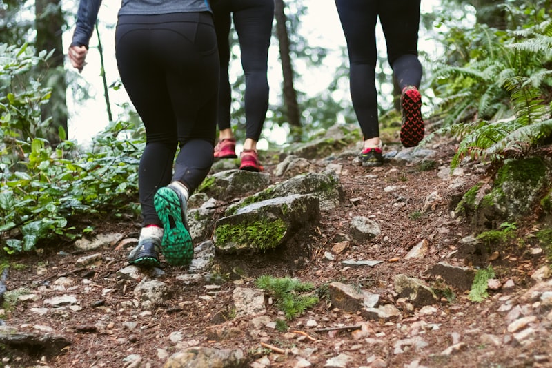 Three people in athletic leggings hiking uphill on a rocky forest trail